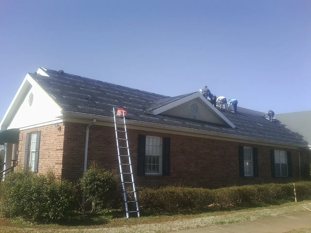 Crew tearing shingles off a brick ranch roof with a ladder set — Emergency Roof Repair work by our crew in Bradford